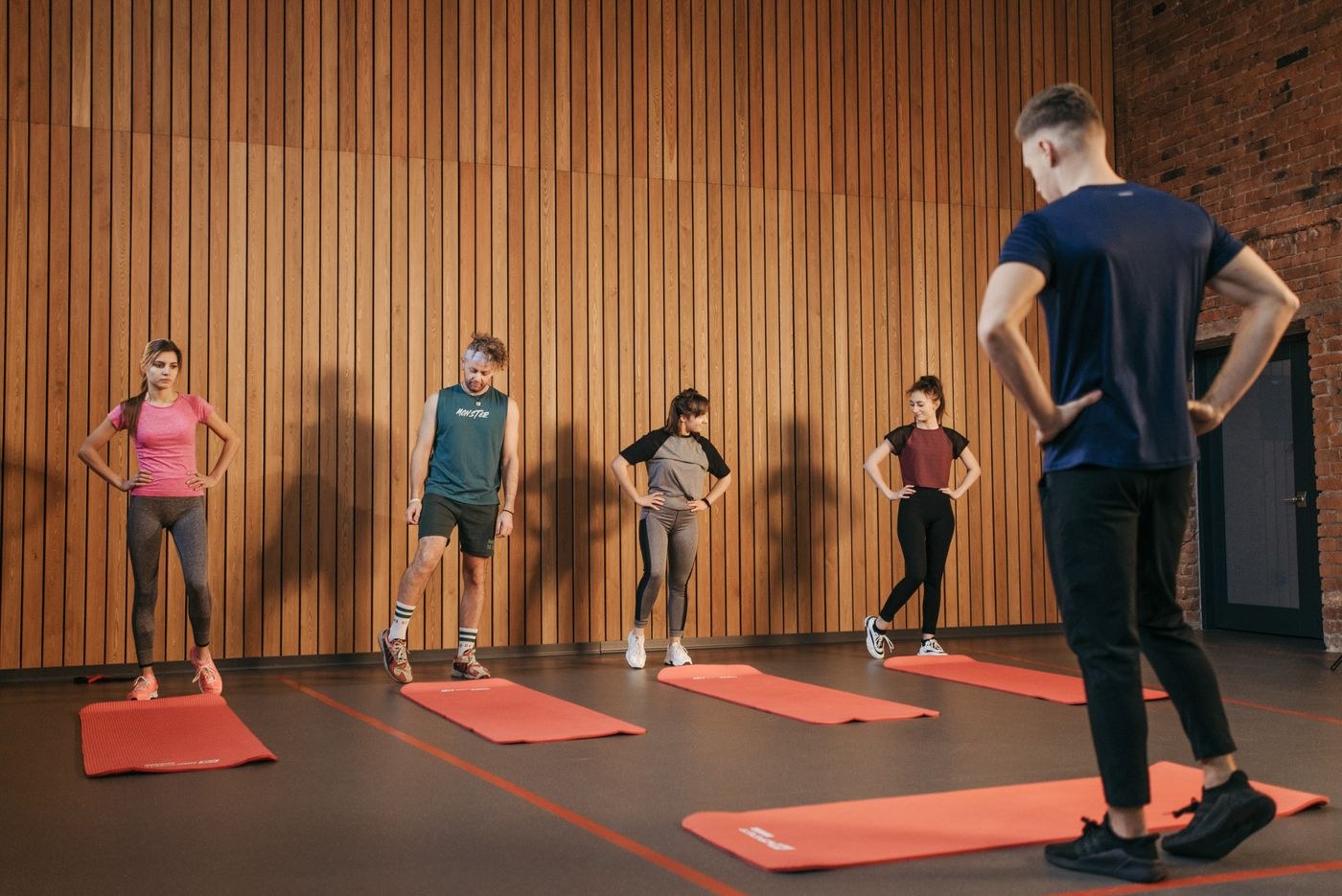 Participants listening to an instructor beside exercise mats in a studio.