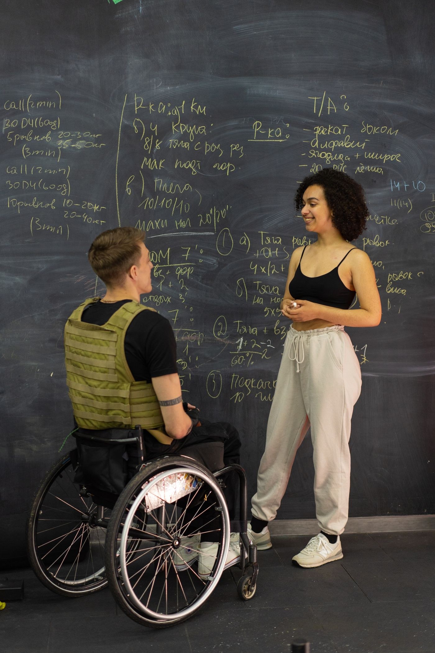 A coach and a wheelchair user discussing training beside a board.