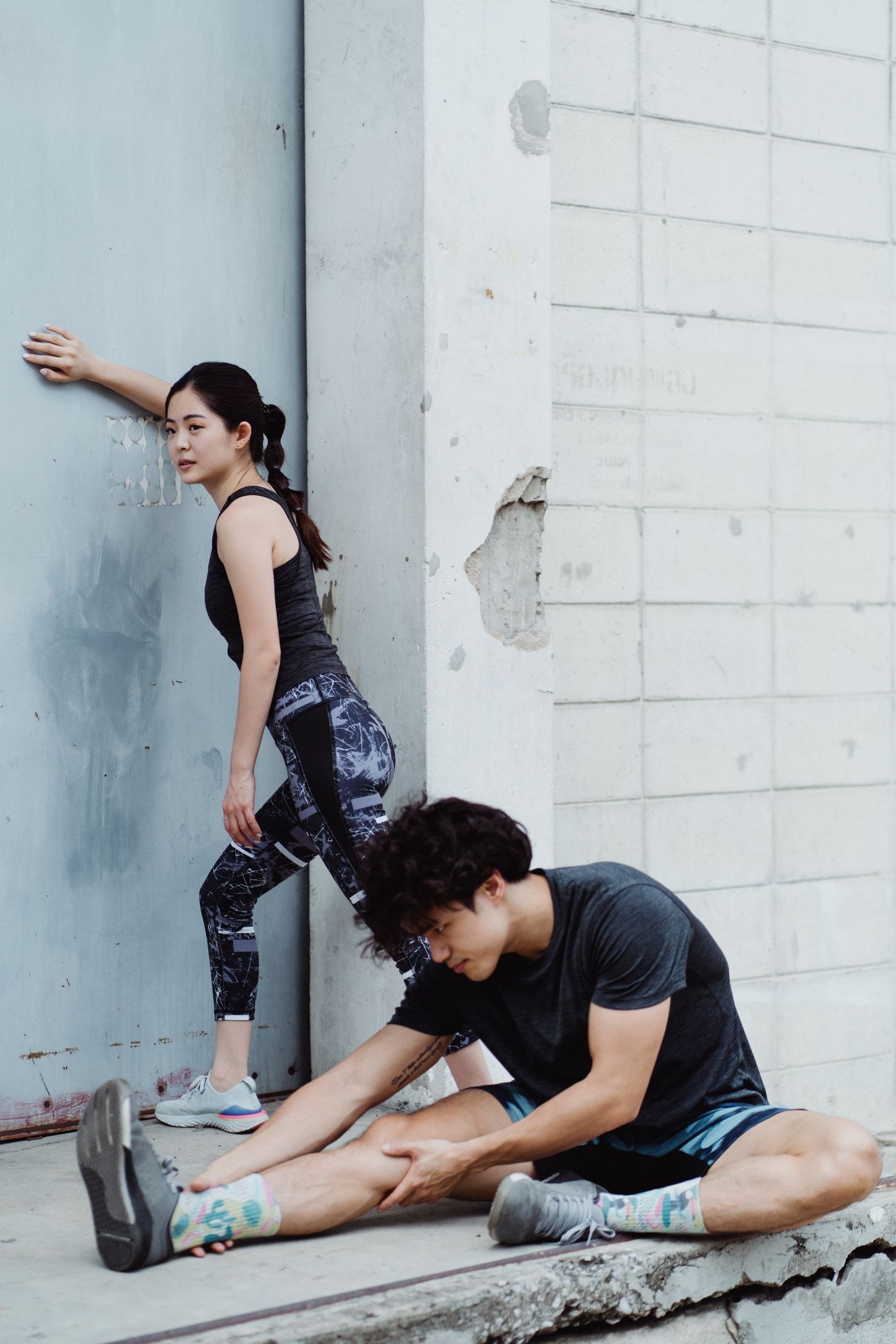 Two adults stretching beside a wall after outdoor activity.