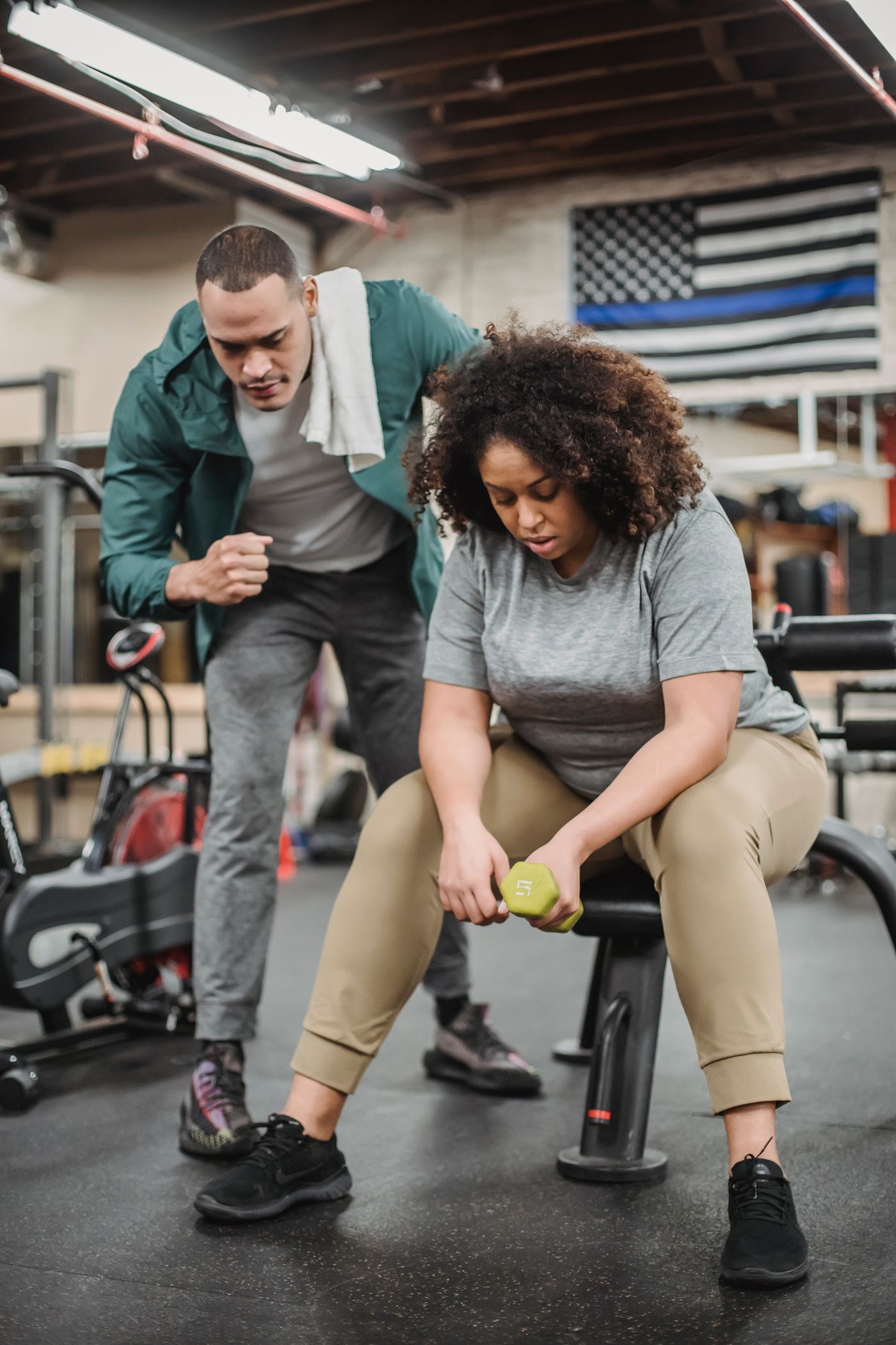 A trainer speaking with a woman seated on a gym bench.
