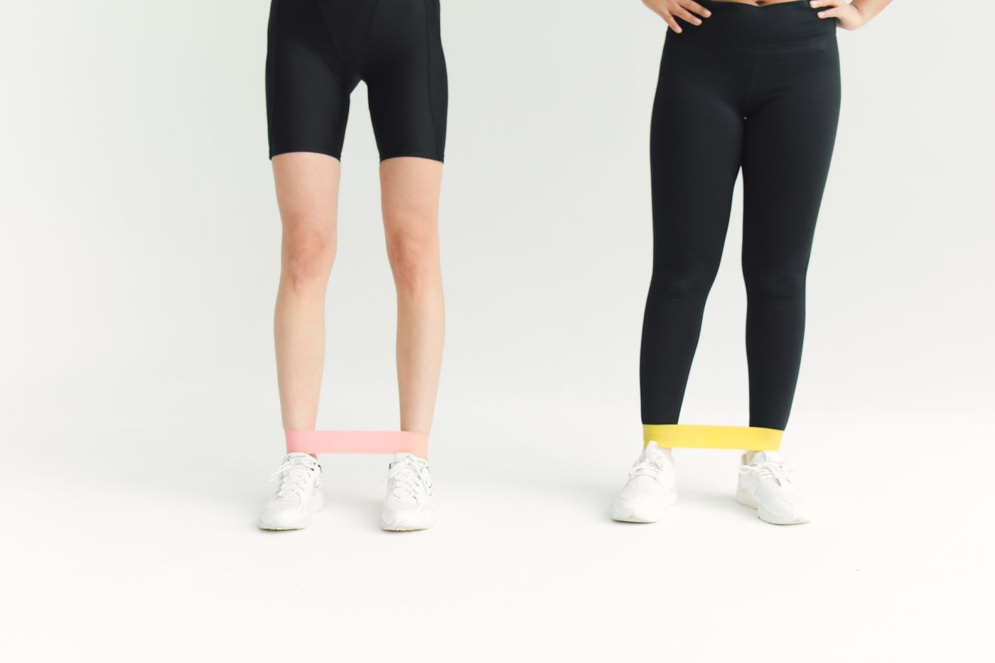 Two people standing with light resistance loops around their lower legs.