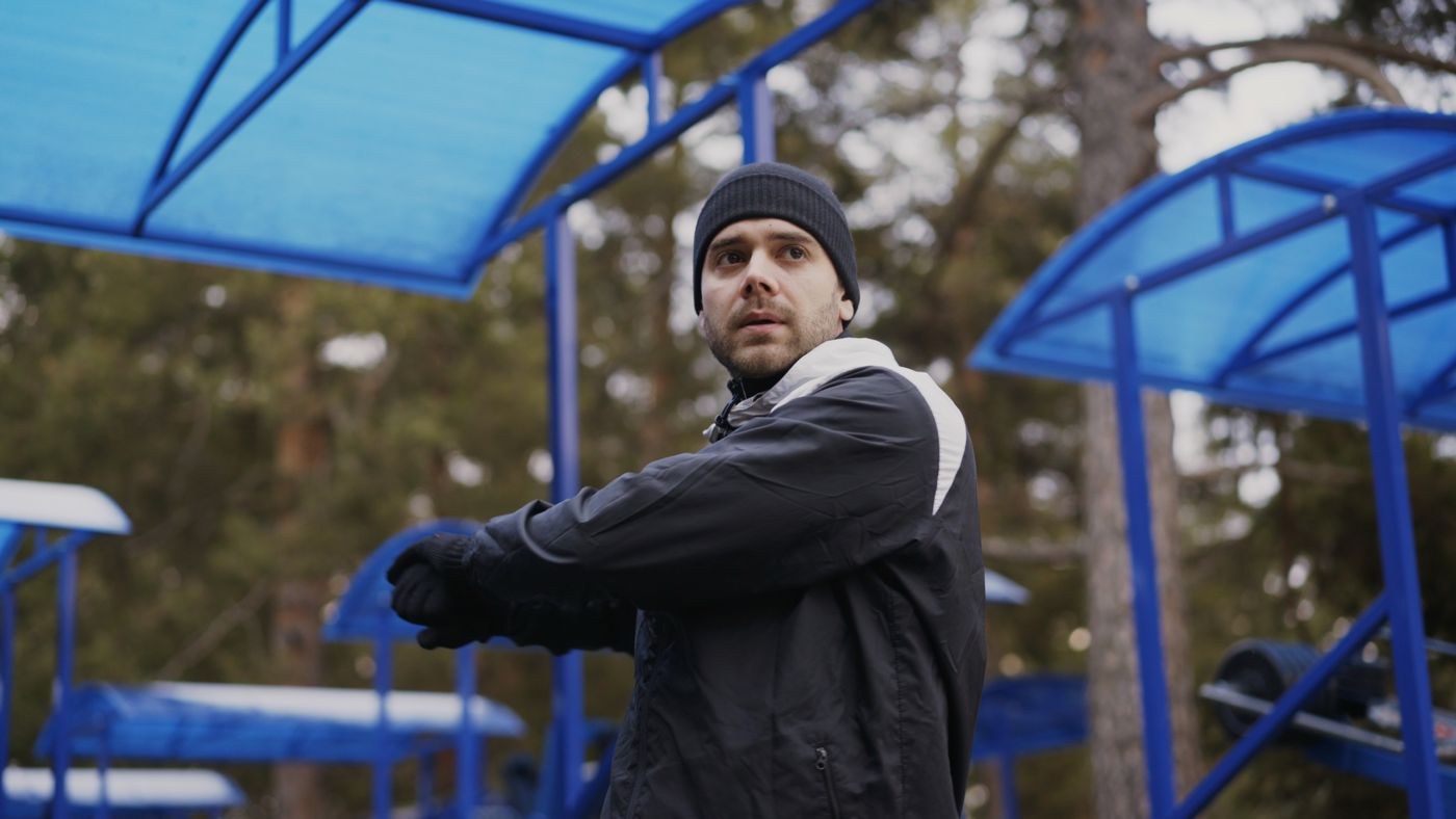 A man warming up outdoors in a hat and zipped training layers.
