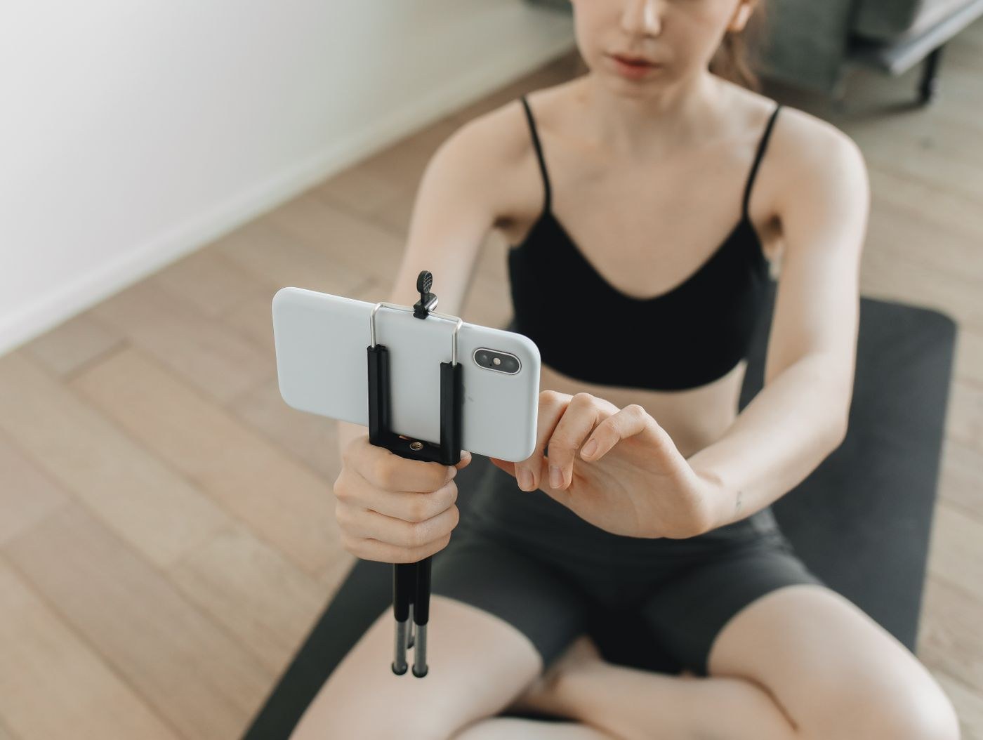 A woman adjusting a smartphone mounted on a small tripod beside a mat.