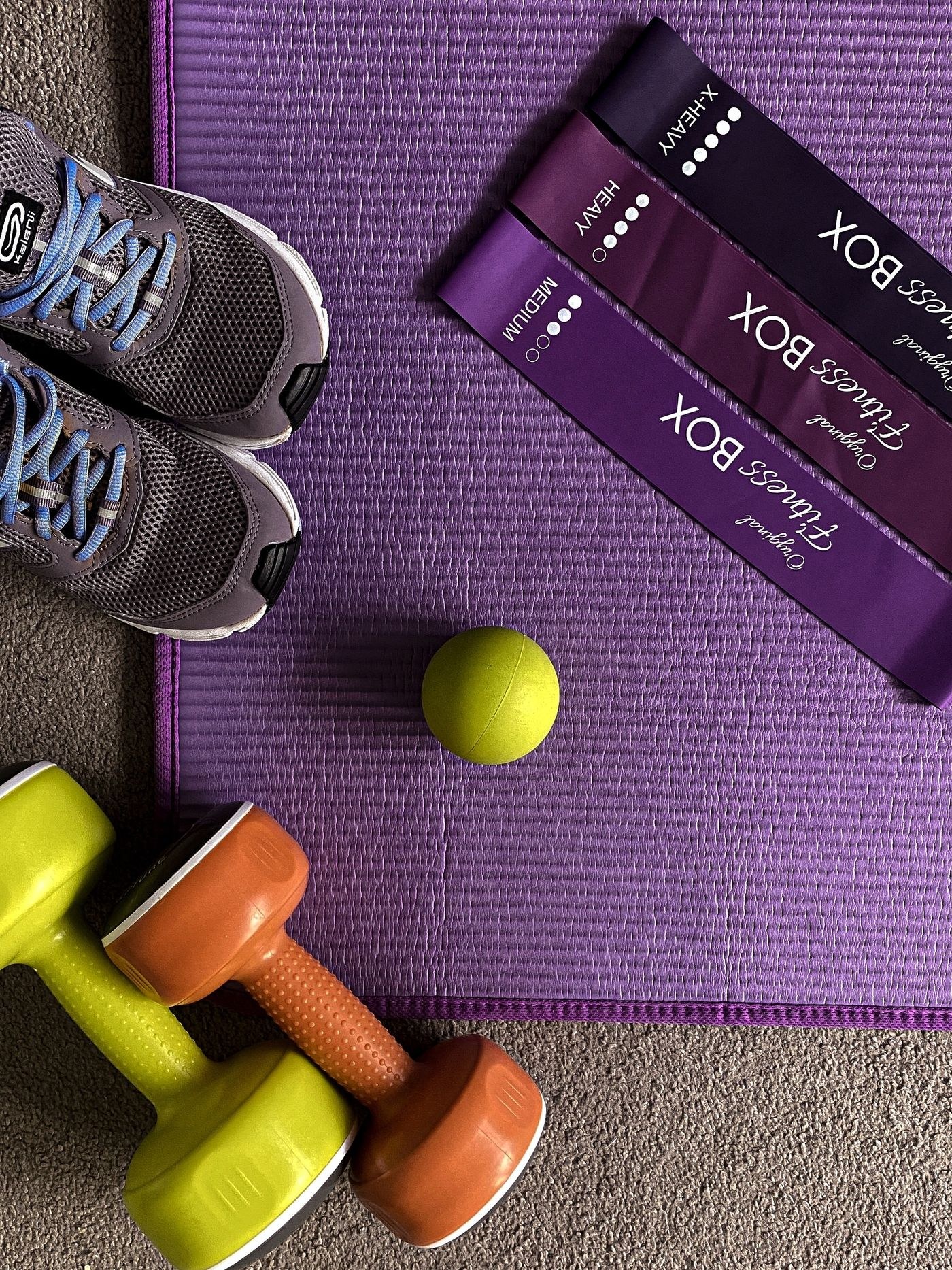 Training shoes, small dumbbells and resistance loops arranged together on a mat.