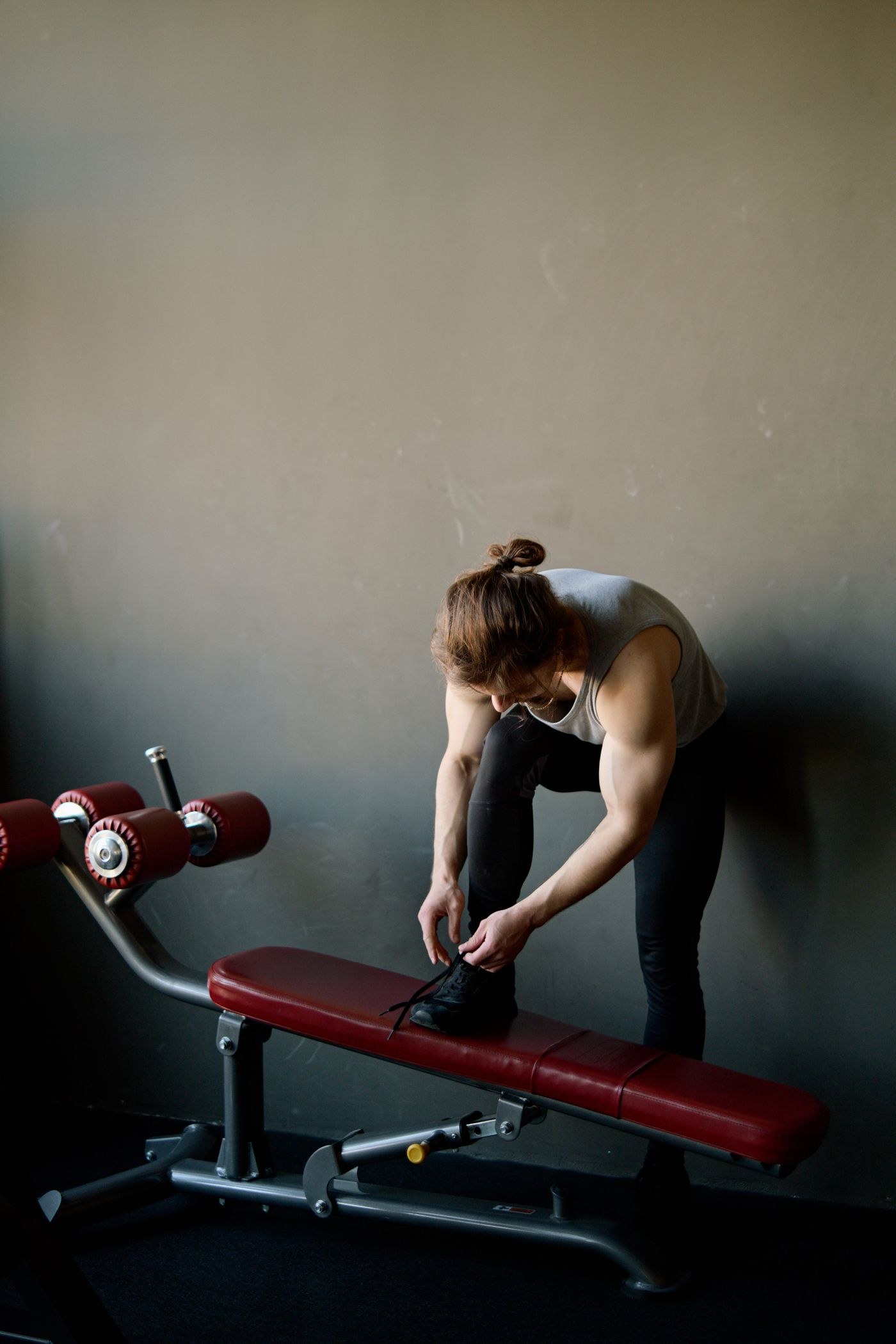 A person adjusting footwear while seated on a gym bench.