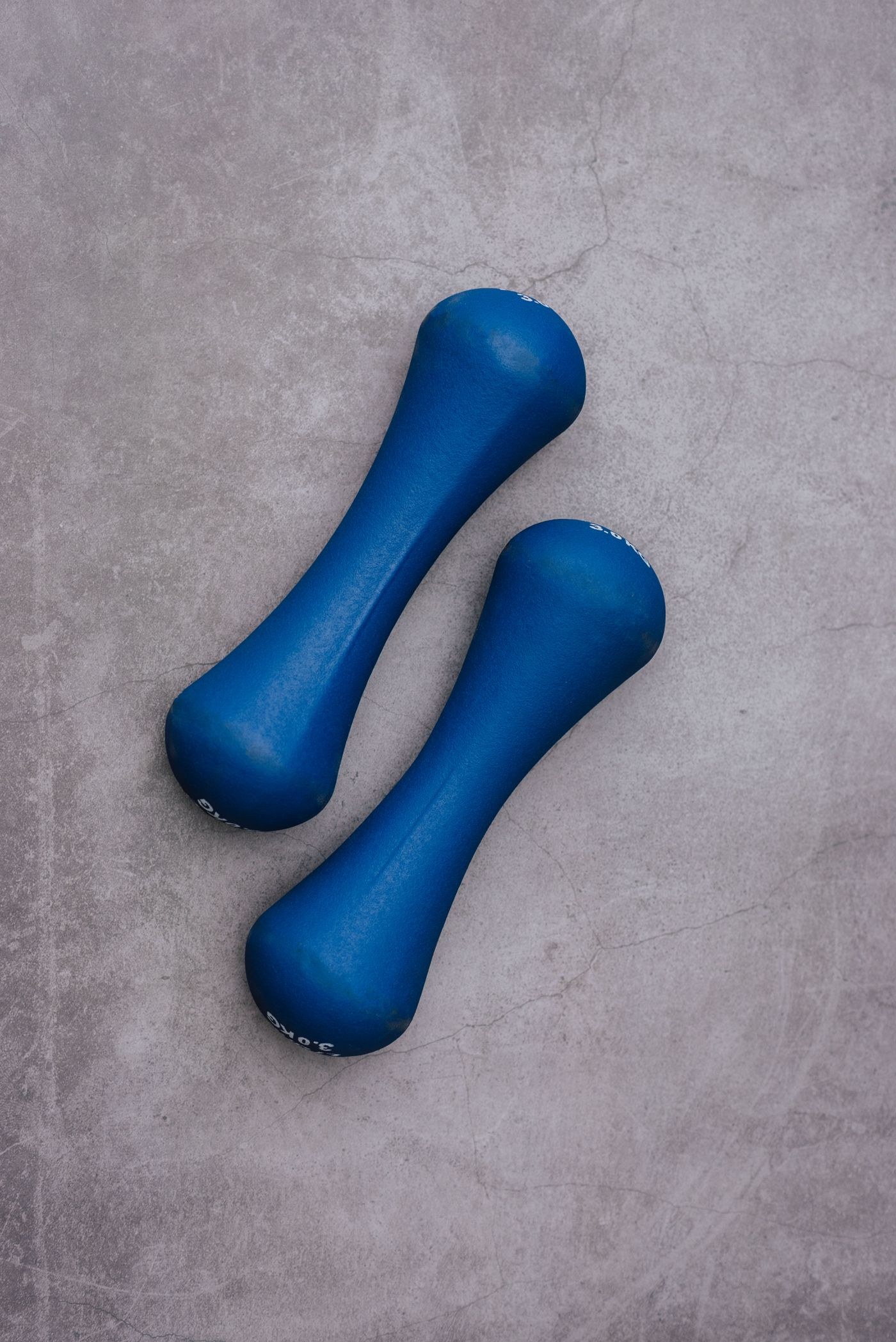 A pair of small blue coated dumbbells on a plain floor.