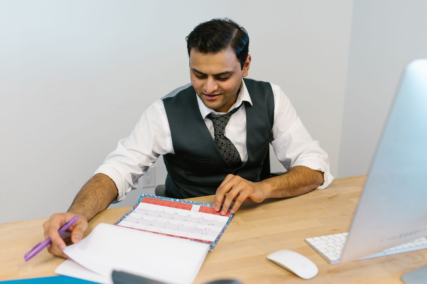 A worker reviewing a paper calendar and notes at a desk.
